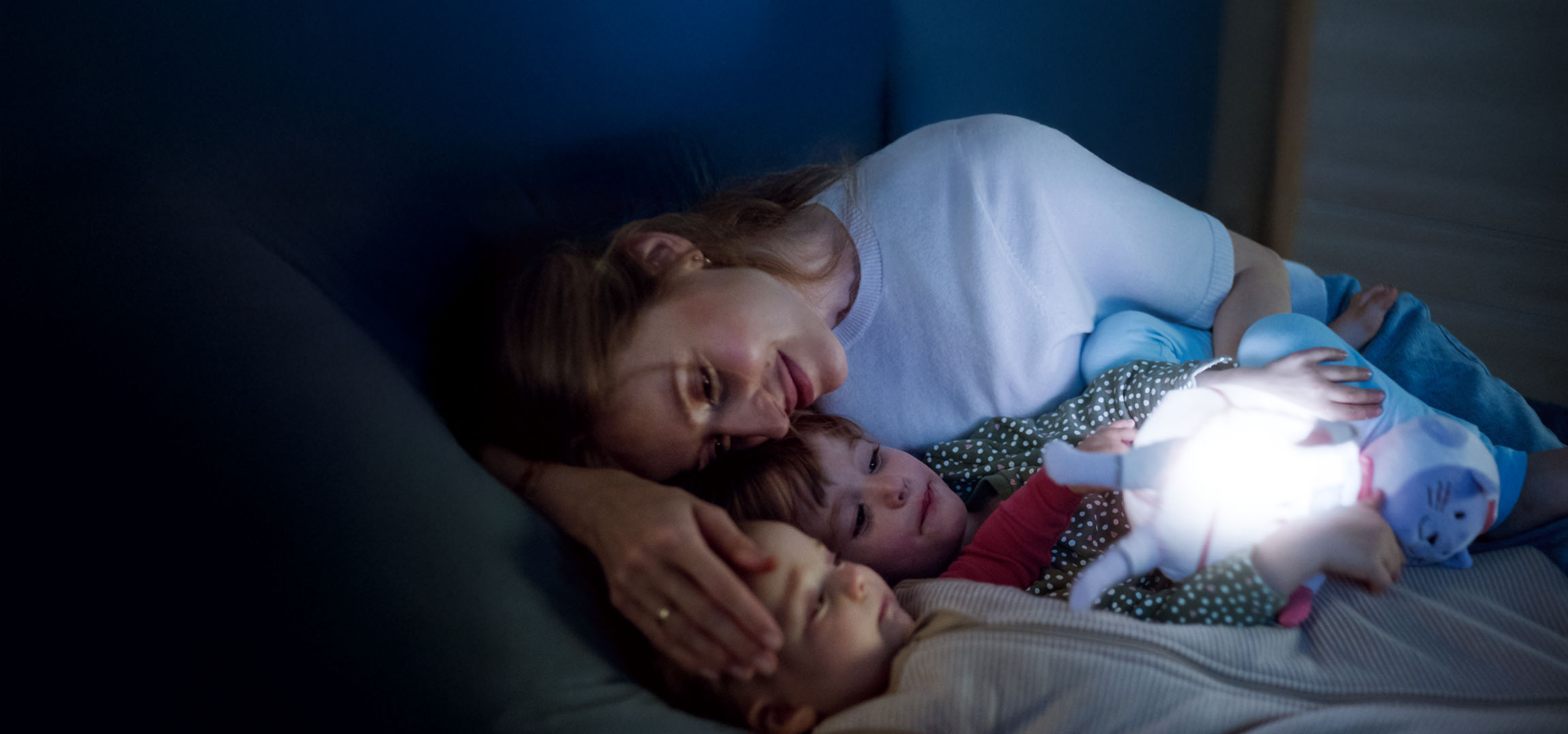 Moeder en twee kinderen in bed met een lichtgevend speeltje