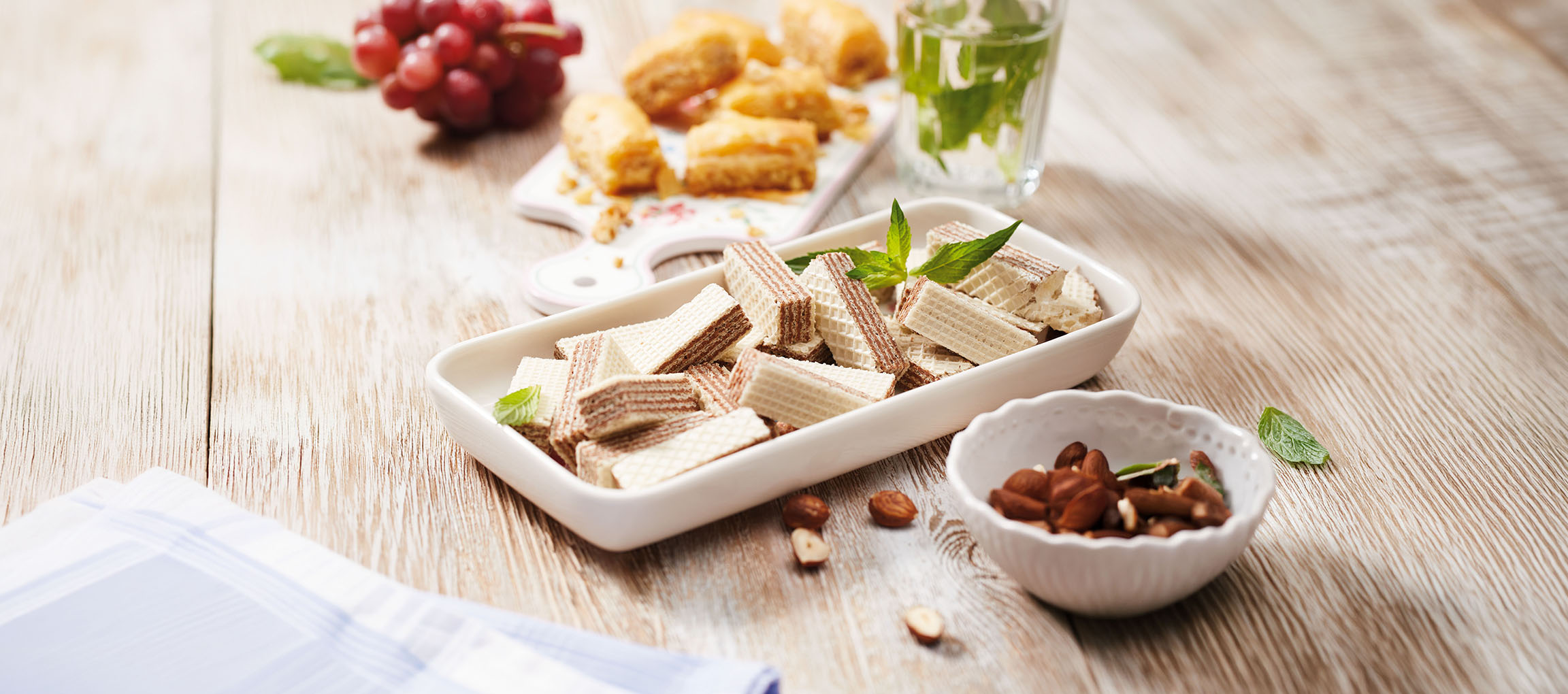 Wafelkoekjes, baklava, druiven en muntwater op een houten tafel.
