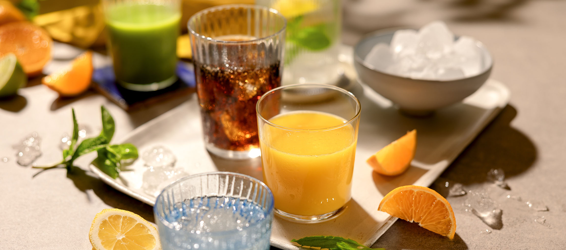 Diverse verfrissende drankjes en fruit op een dienblad, inclusief sinaasappelsap en koolzuurhoudende dranken.