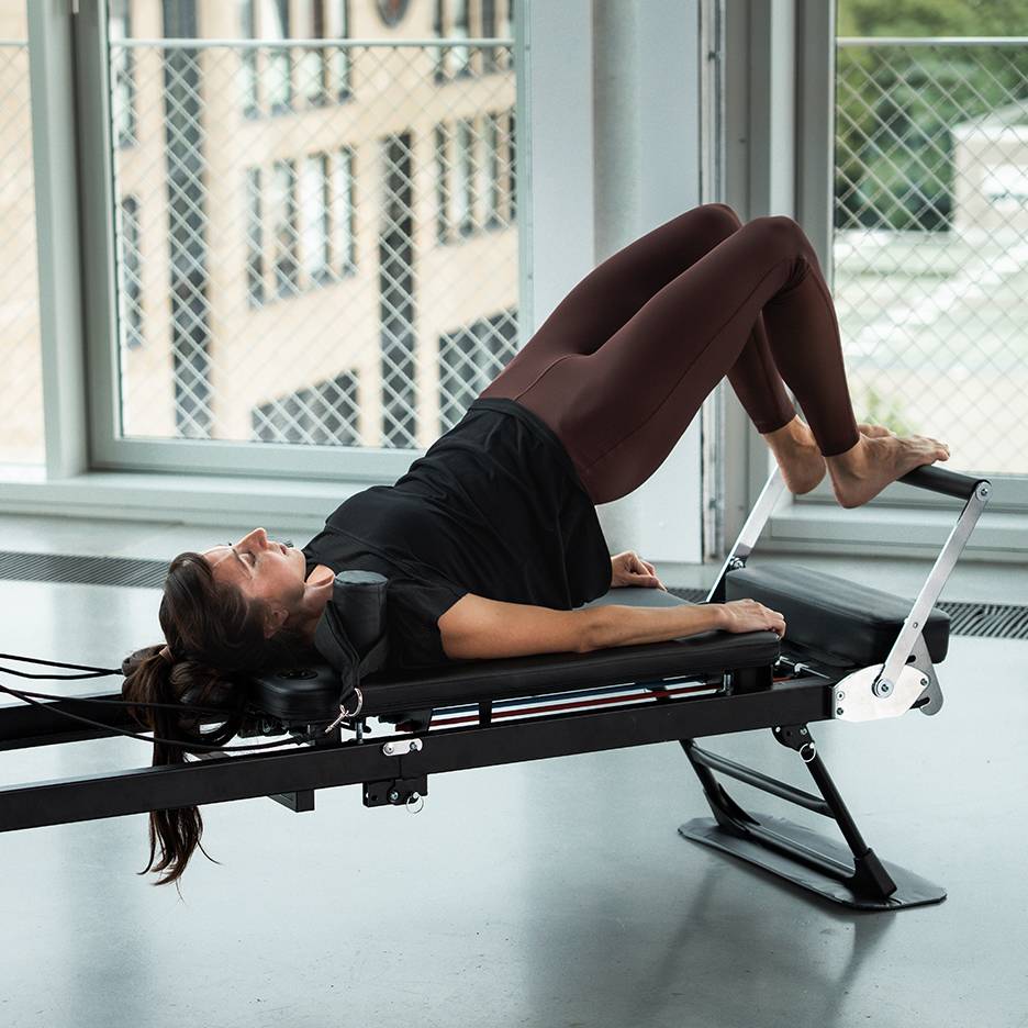 Vrouw doet Pilates op een reformer machine, benen omhoog.