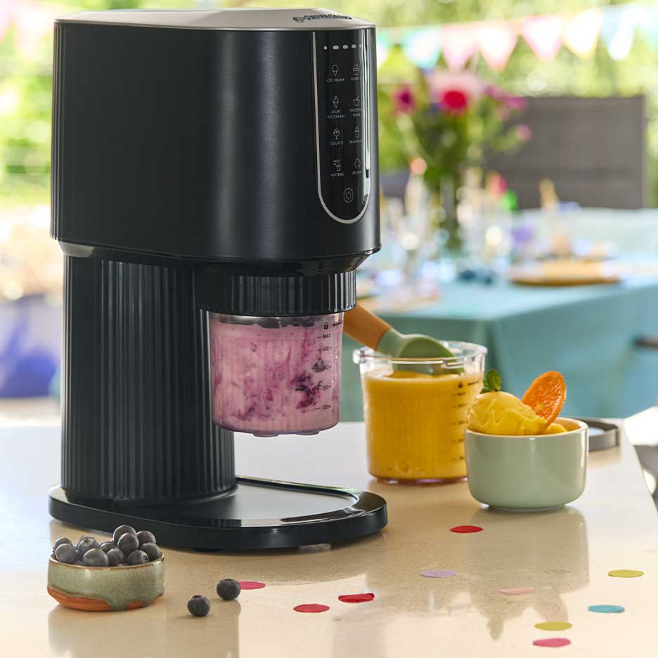 Zwarte ijsmachine met paars ijs, omringd door mango-ijs en bosbessen.