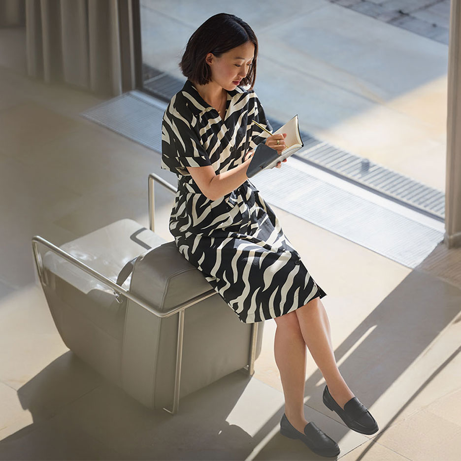 Vrouw in een jurk met zebraprint en loafers, schrijvend in een notitieboekje.
