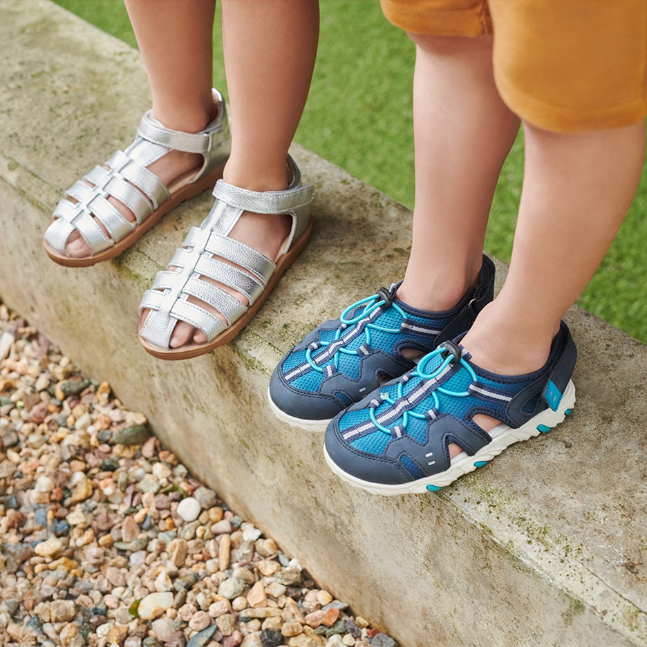 Twee paar kindersandalen: zilverkleurige en blauwe, op een stoeprand.