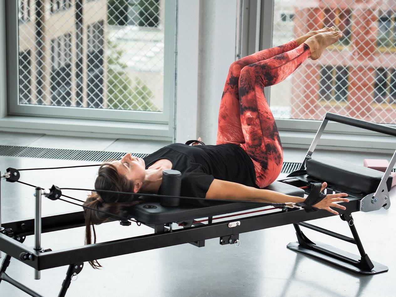Vrouw doet Pilates op een reformer, in een rood-zwarte legging