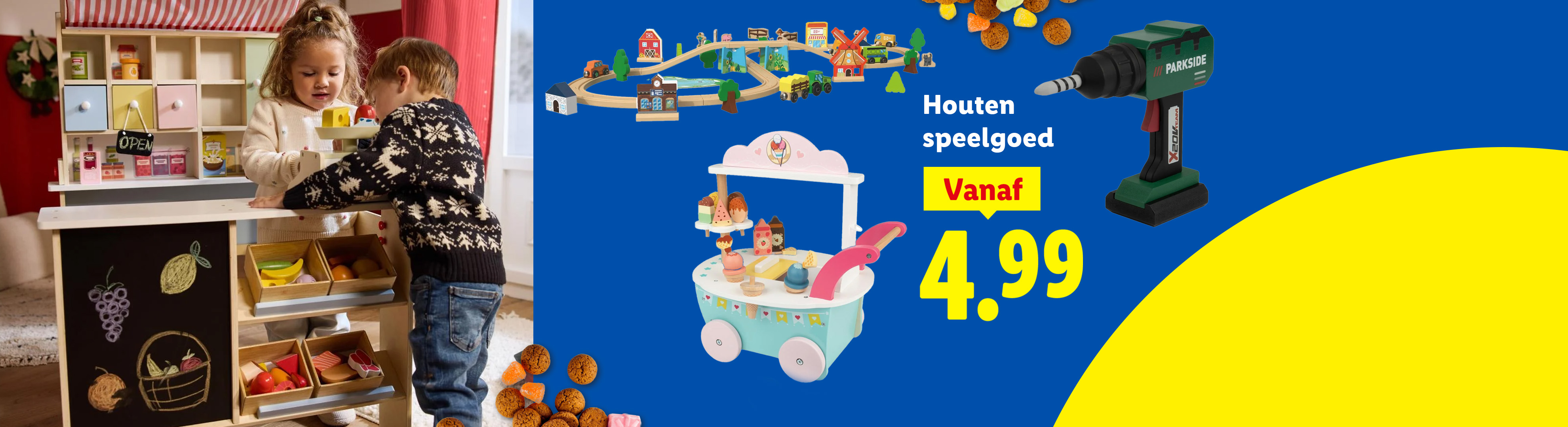 Kinderen spelen met houten speelgoed, waaronder een marktkraam, treinbaan en ijscokar, met een boormachine en pepernoten.