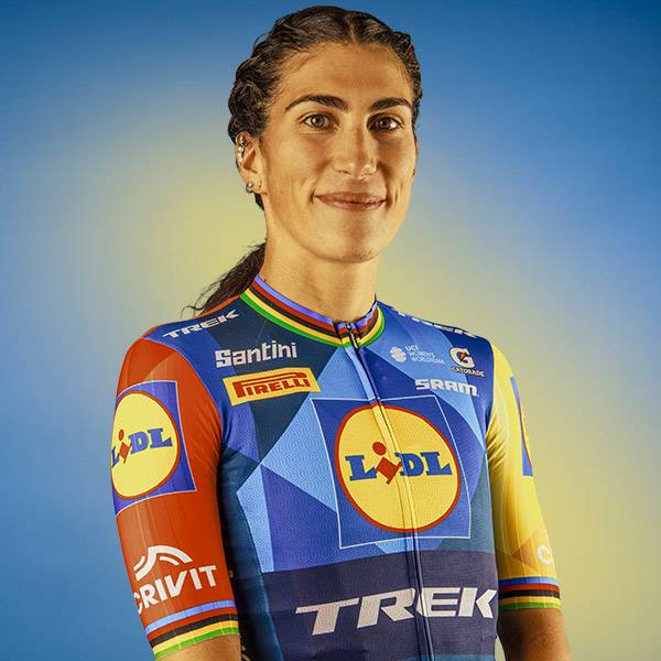 Vrouw in een kleurrijk fietsshirt met geometrische patronen en een supermarktlogo.