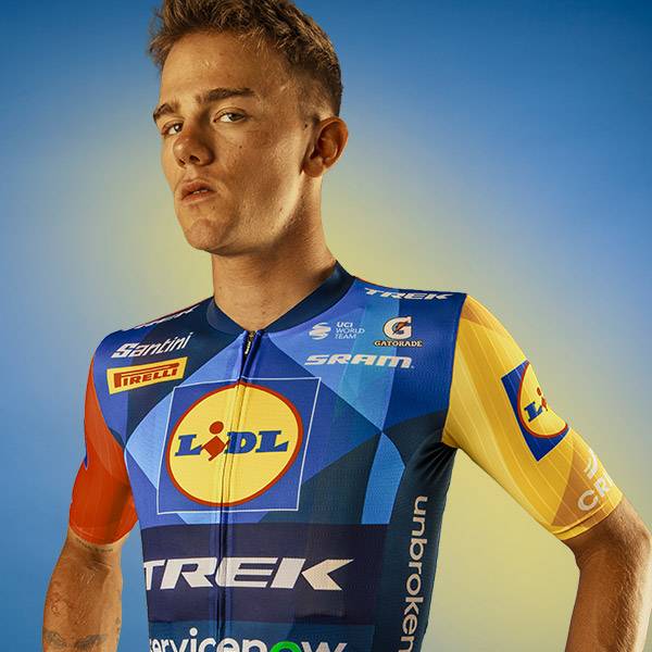 Wielrenner in een blauw en geel fietsshirt met een geometrisch patroon en een supermarktlogo.