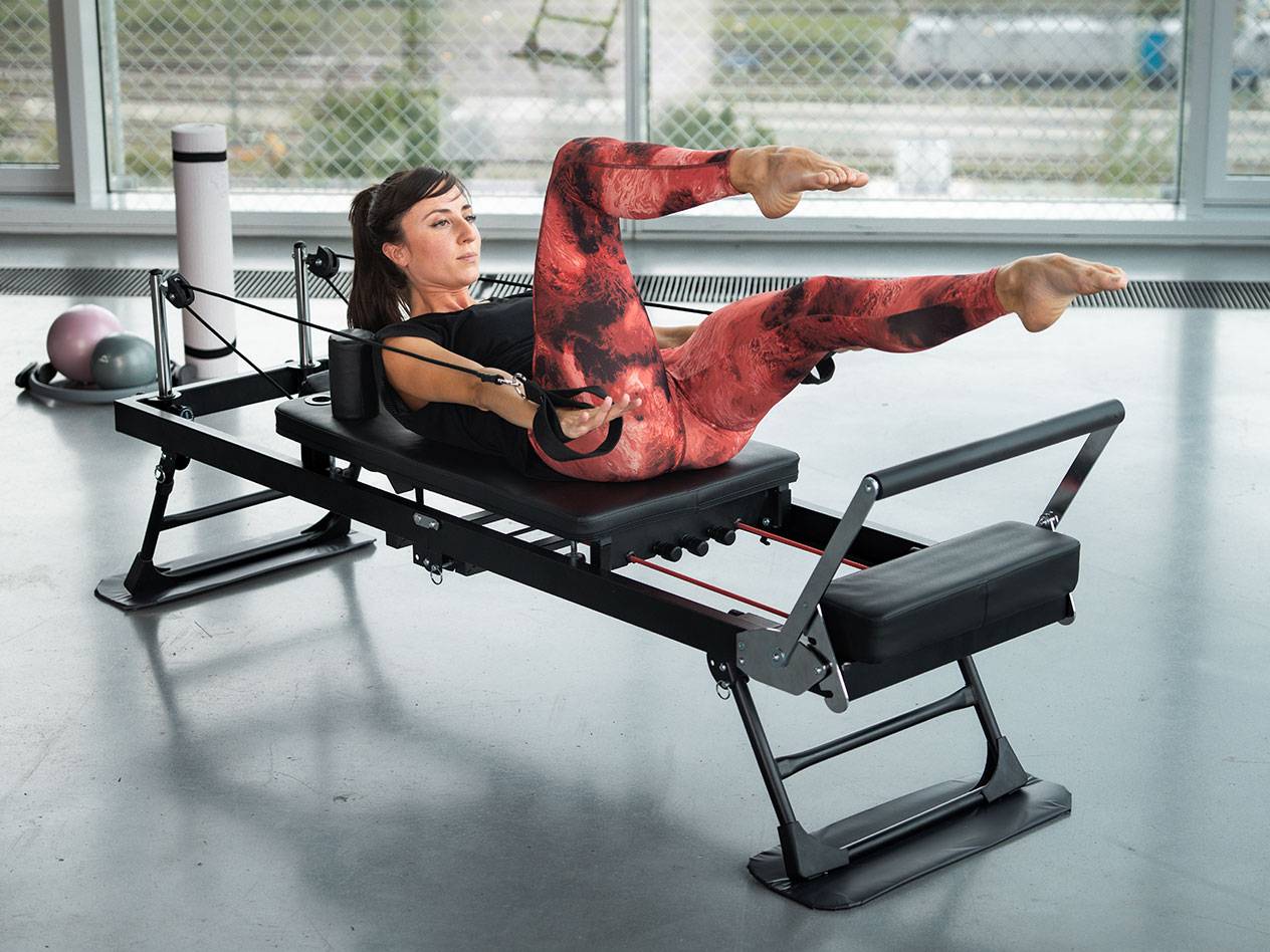 Vrouw doet Pilates op een zwarte Pilatesmachine met rode details.