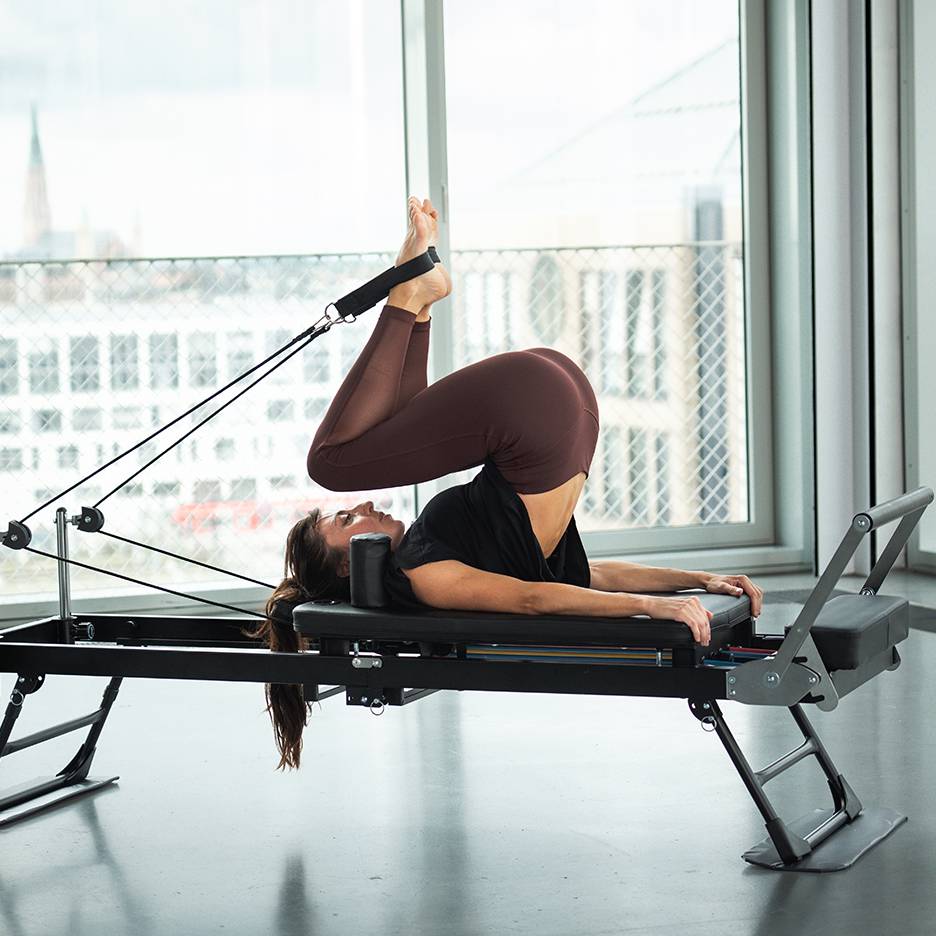 Vrouw doet Pilates op een reformer met benen omhoog en voeten in banden.