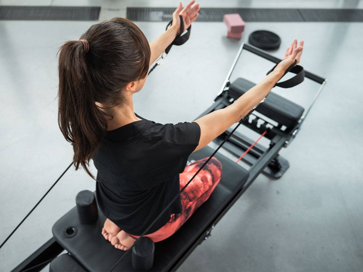 Vrouw doet Pilates op een reformer machine met weerstandsbanden.