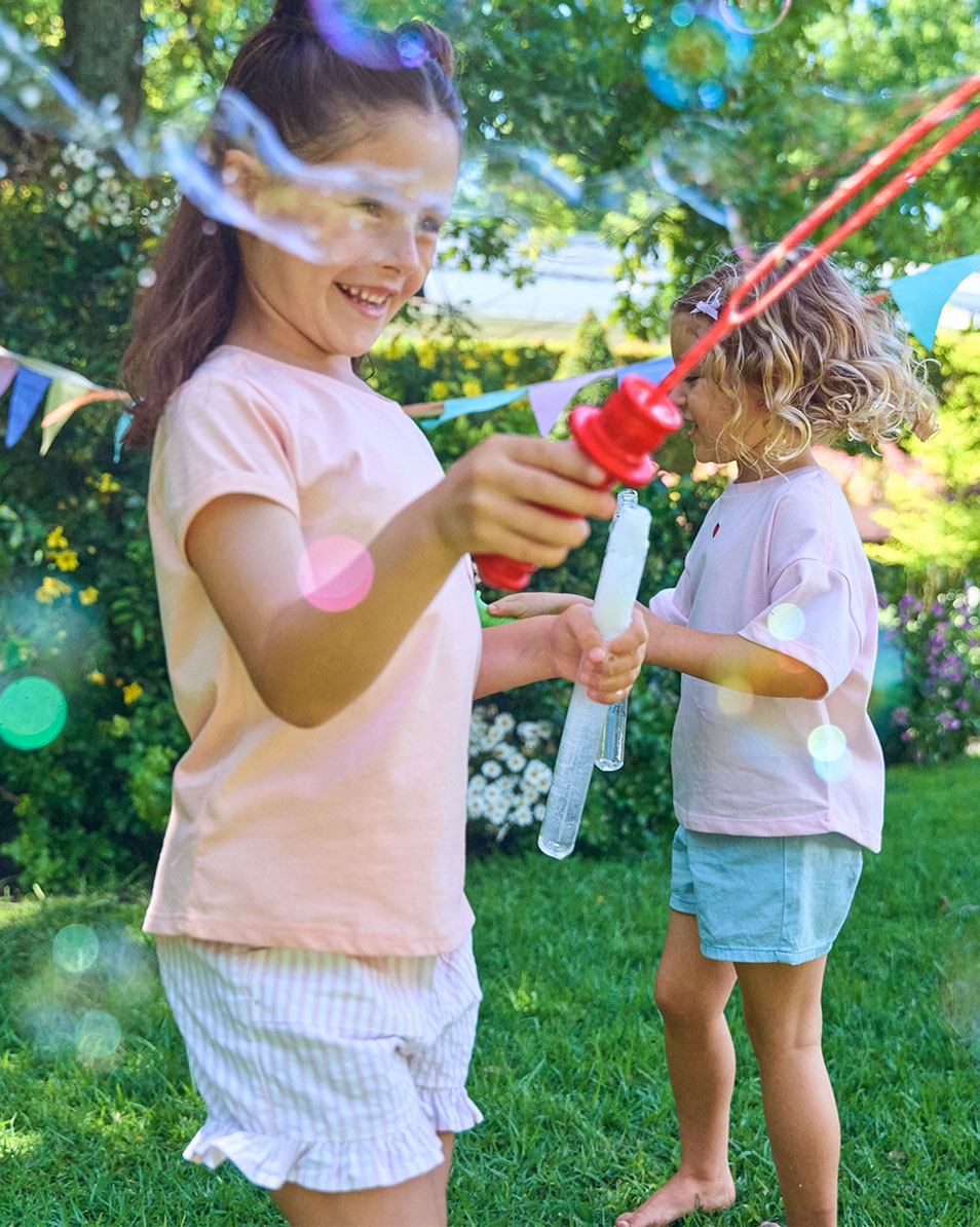 Twee meisjes spelen met bellen in de tuin, gekleed in zomerkleding.