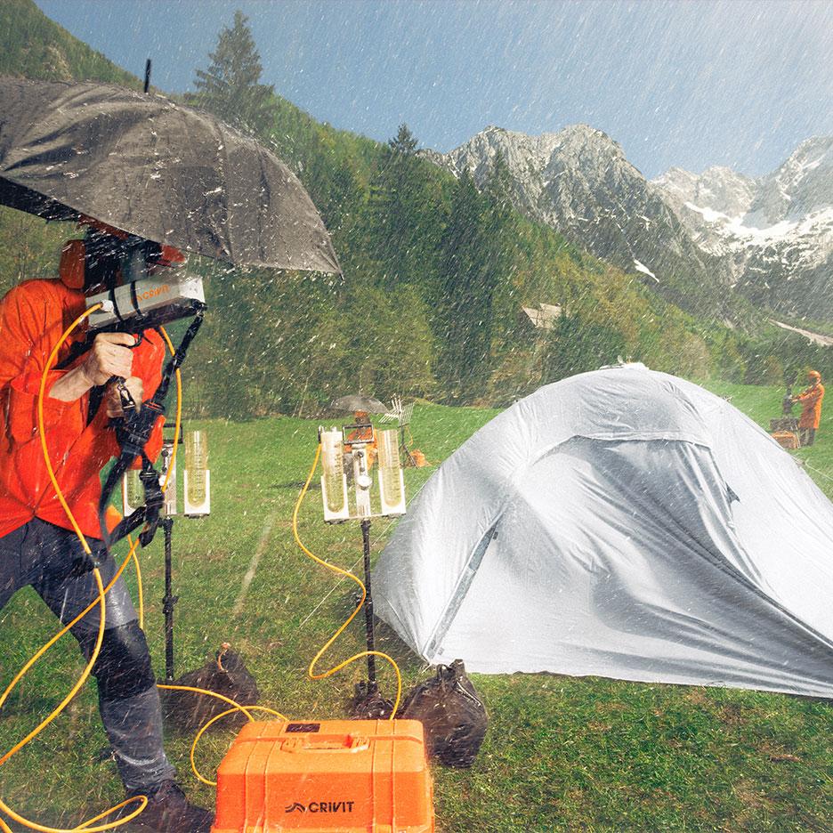 Persoon in regenkleding test kampeeruitrusting in de regen met bergen op de achtergrond.