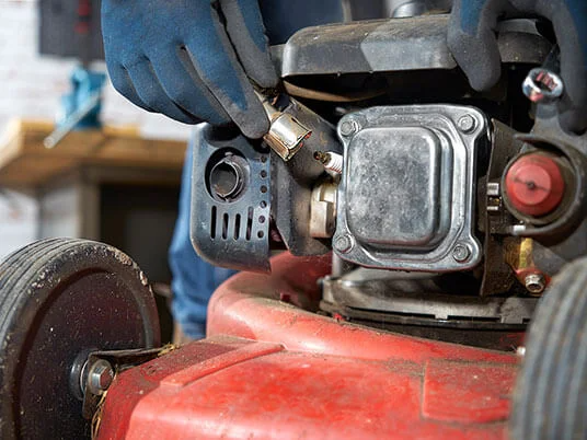 Gehandschoende handen vervangen de bougie van een rode grasmaaier.