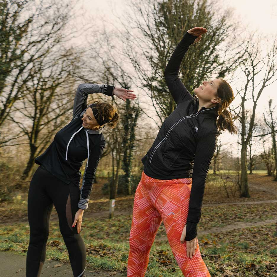 Twee vrouwen in sportkleding rekken zich buiten uit.