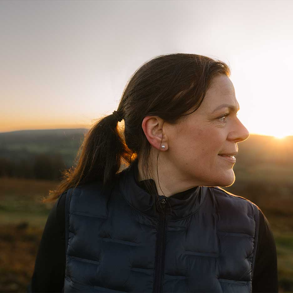 Vrouw in zwart vest en zwarte trui bij zonsondergang.