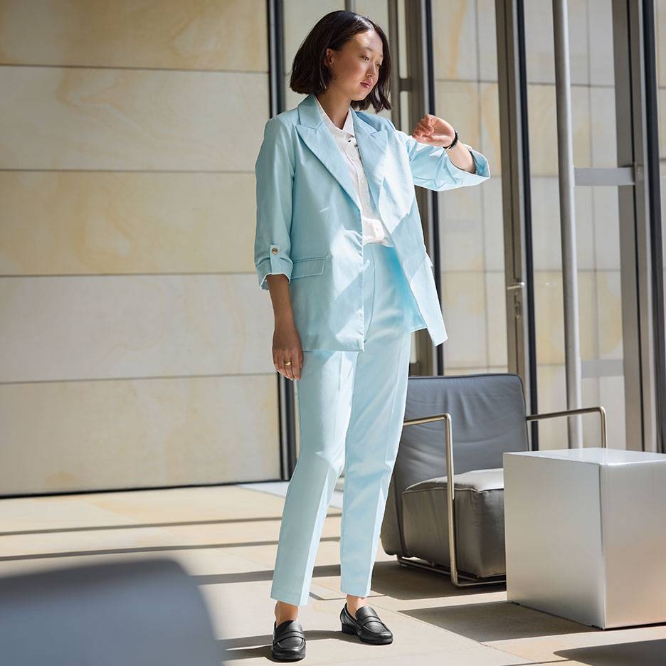 Vrouw in lichtblauw pak met blazer en broek, draagt zwarte loafers.