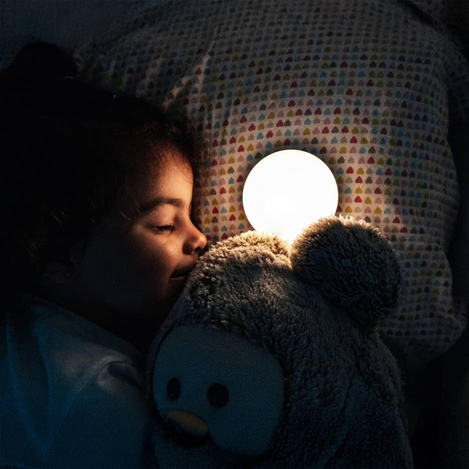 Meisje slaapt met knuffel en lichtgevend nachtlampje.