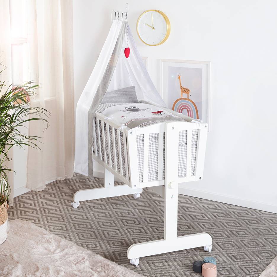 Witte babywieg met hemel en schattige beddengoedpatronen, in een kamer met tapijt.
