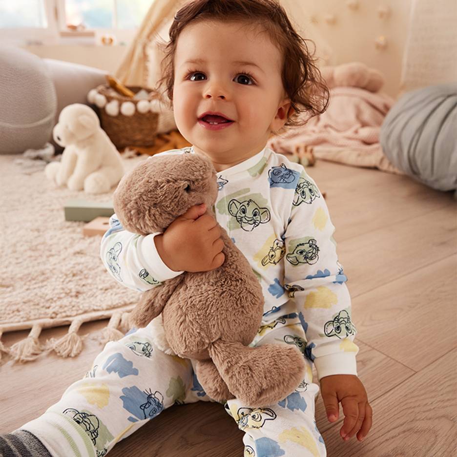 Blije baby in Lion King pyjama met bruin knuffeldier.