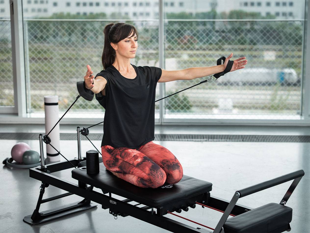 Vrouw doet Pilates op een reformer met weerstandsbanden.