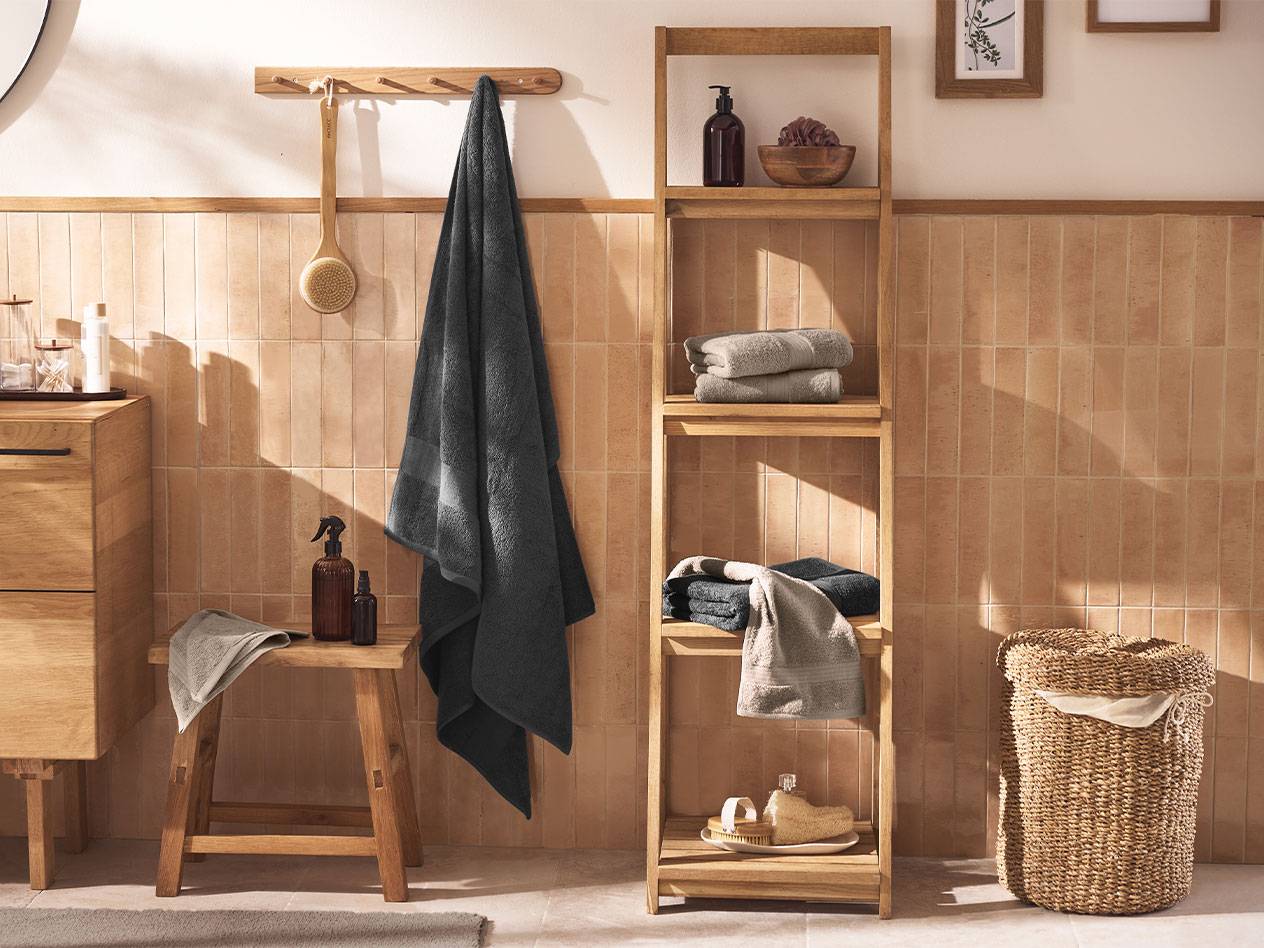 Badkamer met grijze handdoeken, houten planken en badkameraccessoires.