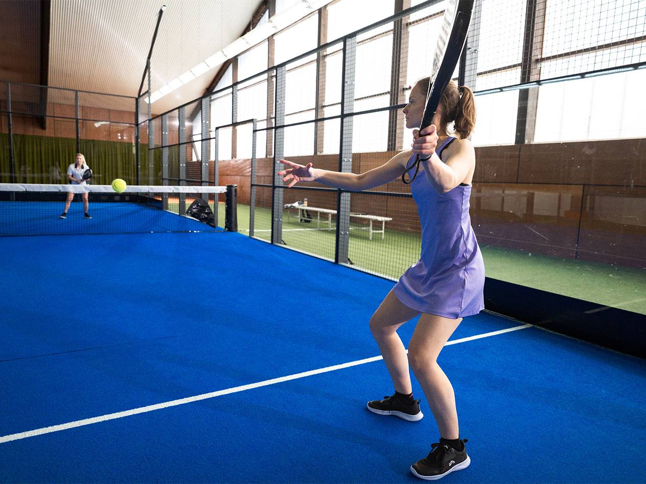 Vrouw in een paarse sportjurk speelt padel op een blauw veld.