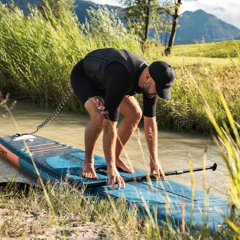 Man in wetsuit en zwemvest bereidt zich voor op stand-up paddleboarden op een rivier.