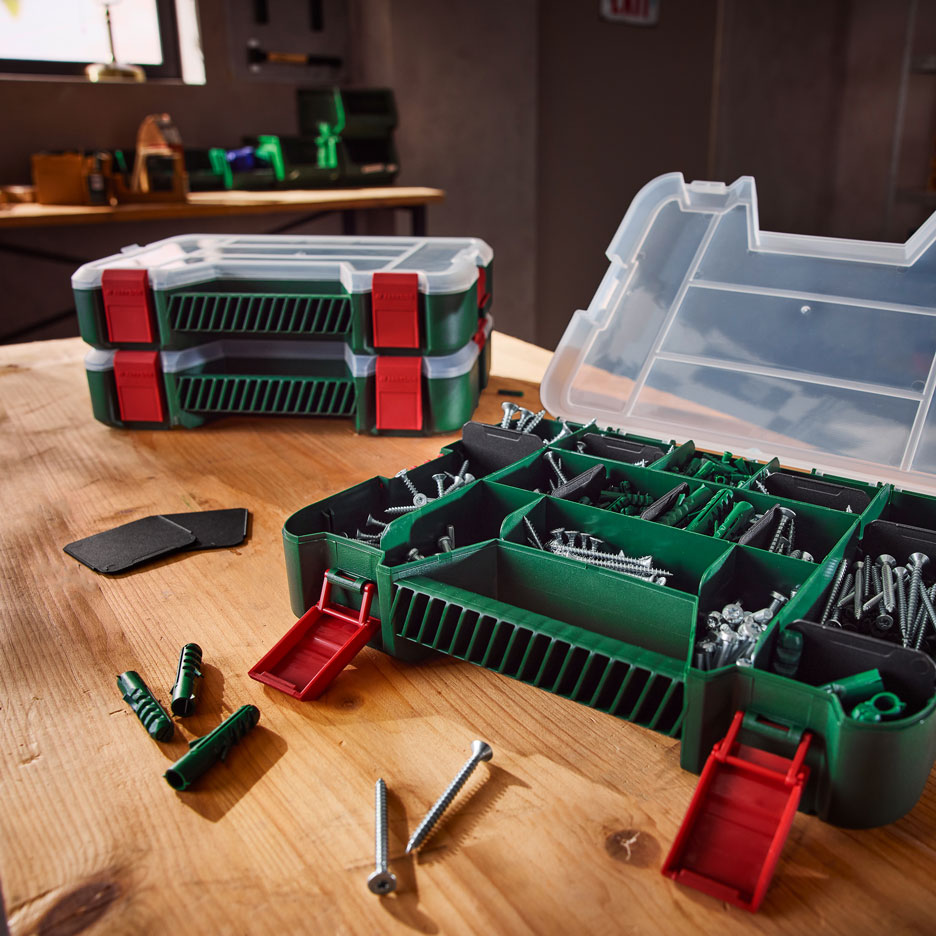 Groene gereedschapsorganizers met schroeven en pluggen op een houten werkbank.
