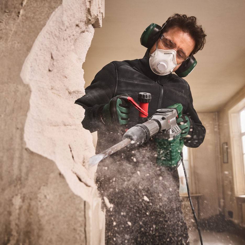 Man met sloophamer en beschermende kleding sloopt een muur.