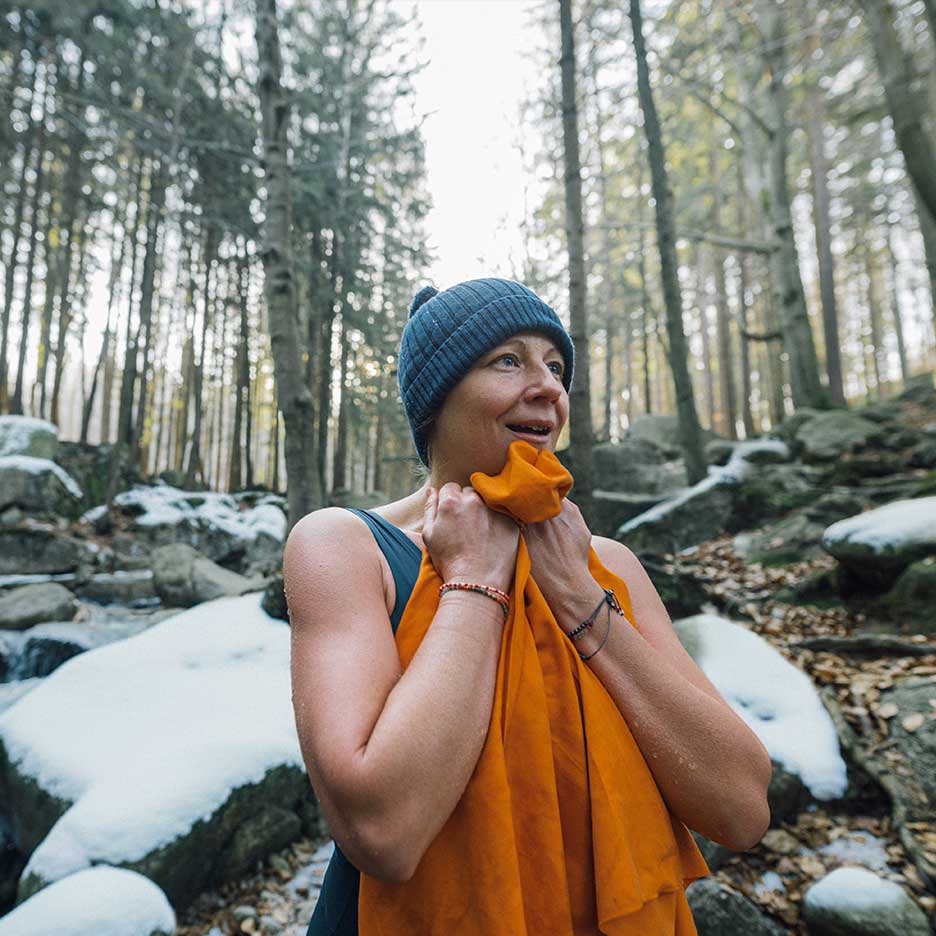 Vrouw in muts en badpak warmt zich op met handdoek in besneeuwd bos.