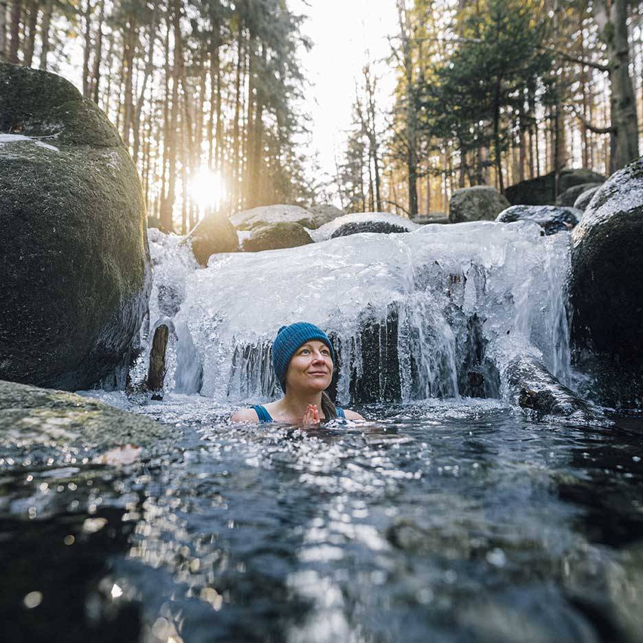 Vrouw in blauwe muts en badpak genietend van een koude duik in een bevroren rivier.