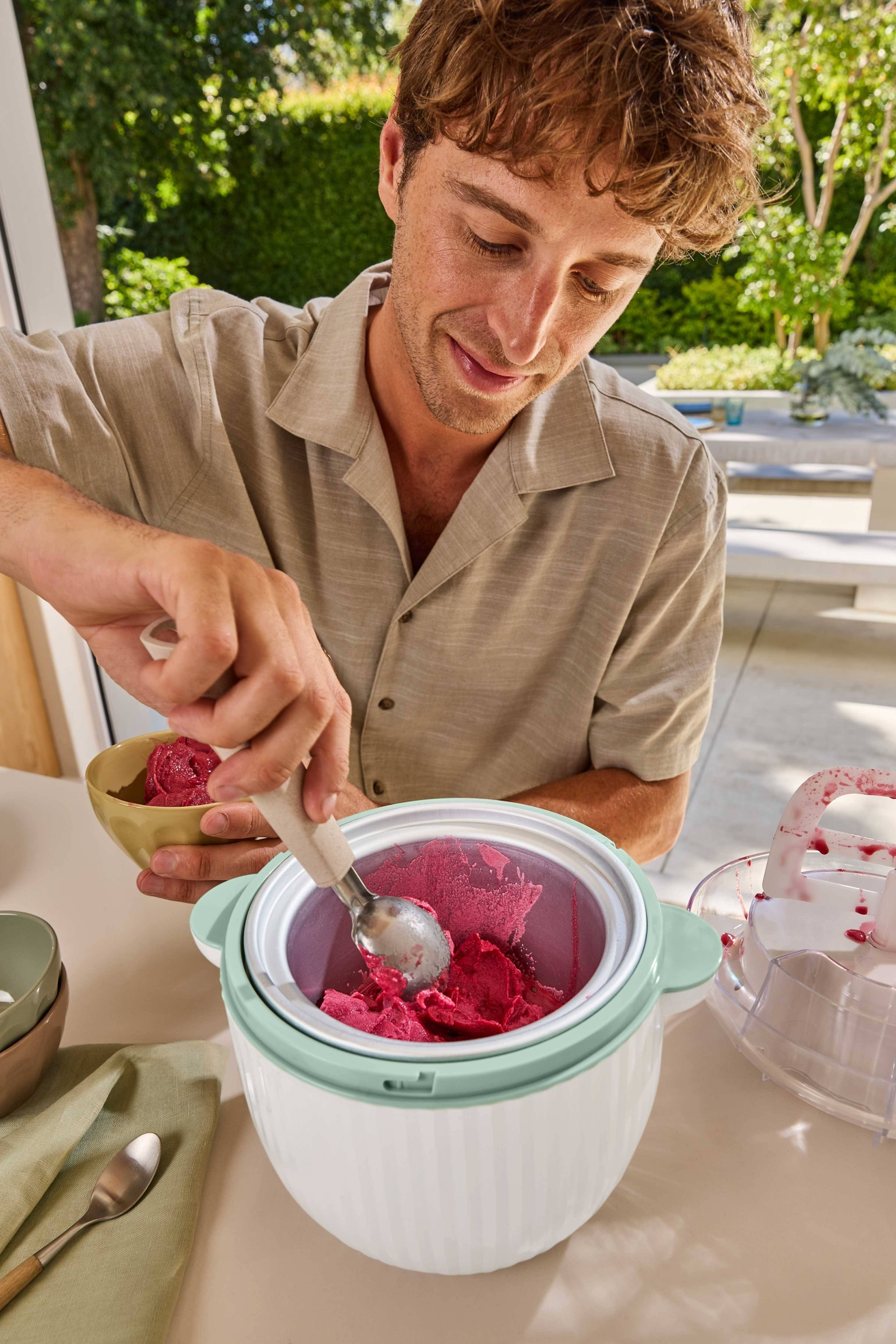 Man schept rode sorbet uit een ijsmachine in een kom.