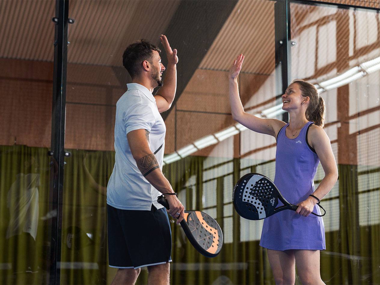 Twee padelspelers, een man en een vrouw, geven elkaar een high-five op de baan.