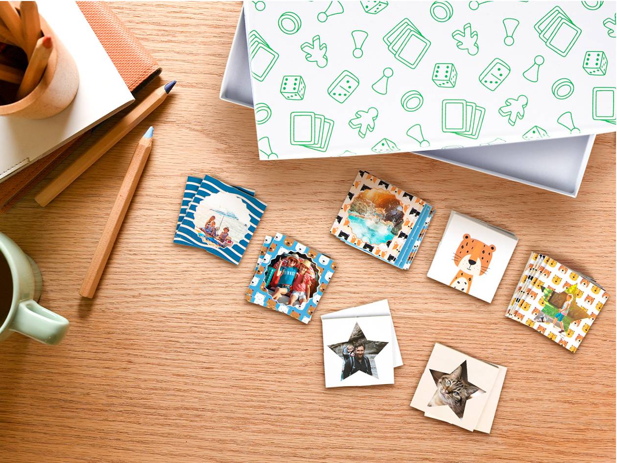 Een houten tafel met een open doos vol bordspeliconen en kleine vierkante fotoboekjes met diverse afbeeldingen.