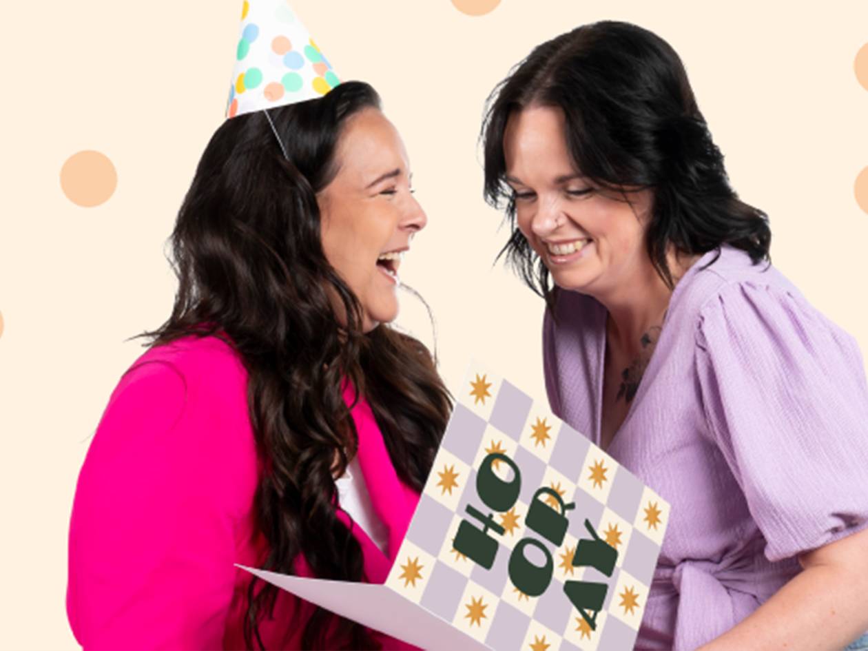 Twee lachende vrouwen met een feestmuts en een 'HOORAY'-kaart.