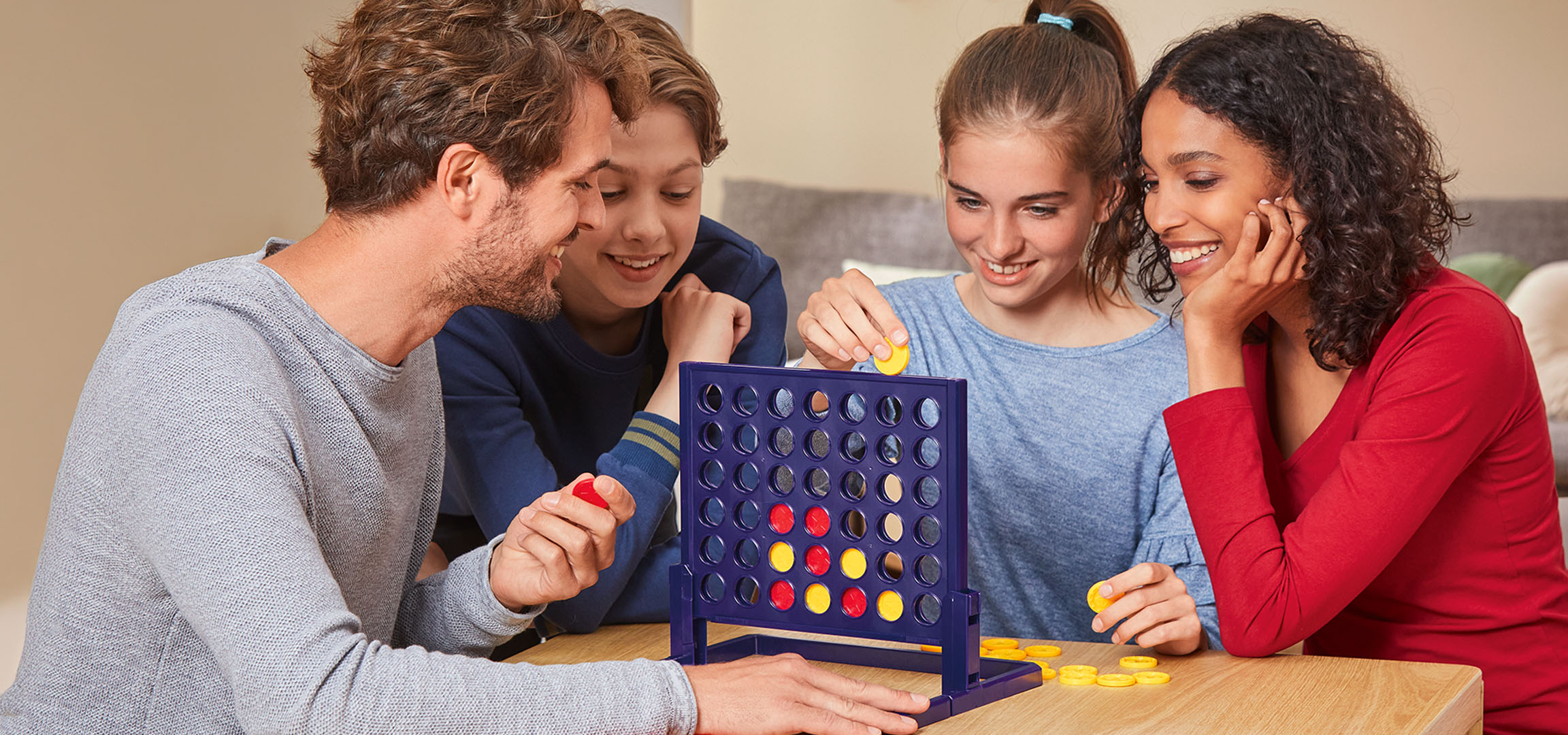 Vier mensen spelen het Connect 4 bordspel aan een houten tafel.