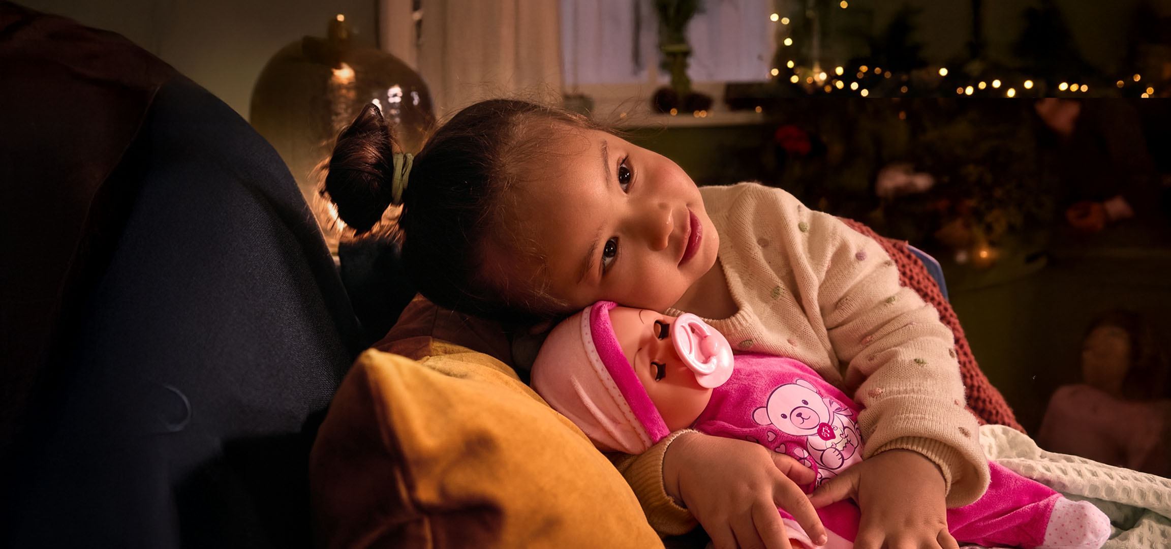 Meisje met pop en speen, knus op een kussen.