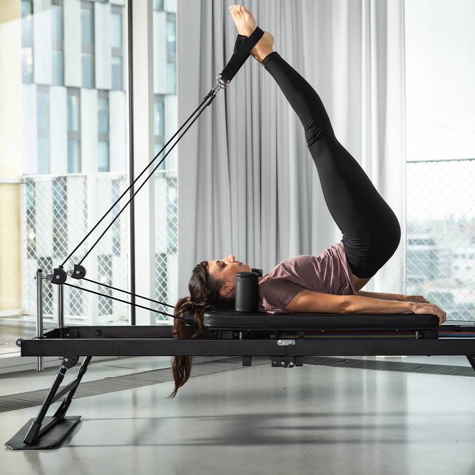 Vrouw doet Pilates op een zwarte Pilates-machine met benen omhoog.