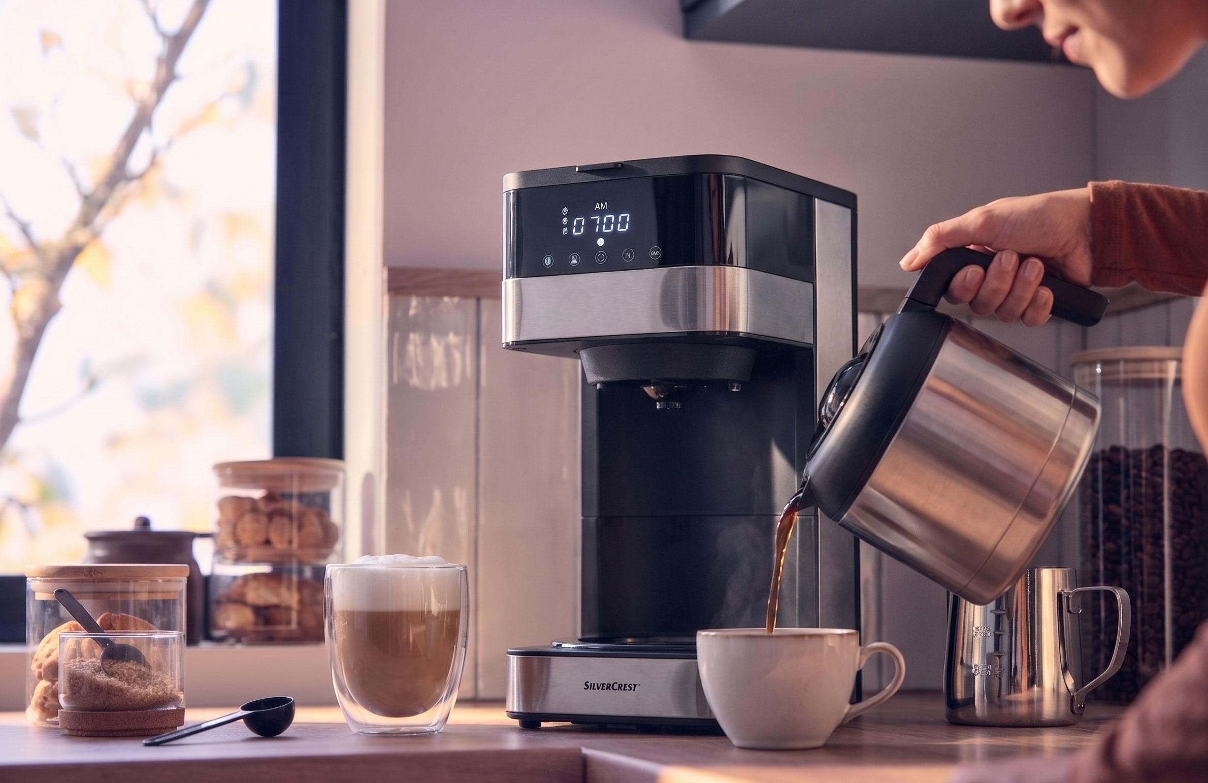 Koffiezetapparaat schenkt koffie in een kopje, met een latte en koekjes op het aanrecht.