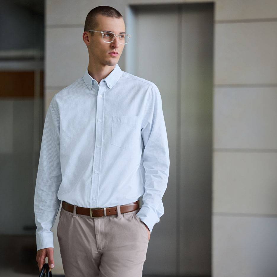 Man in lichtblauw gestreept overhemd en beige broek met bruine riem.