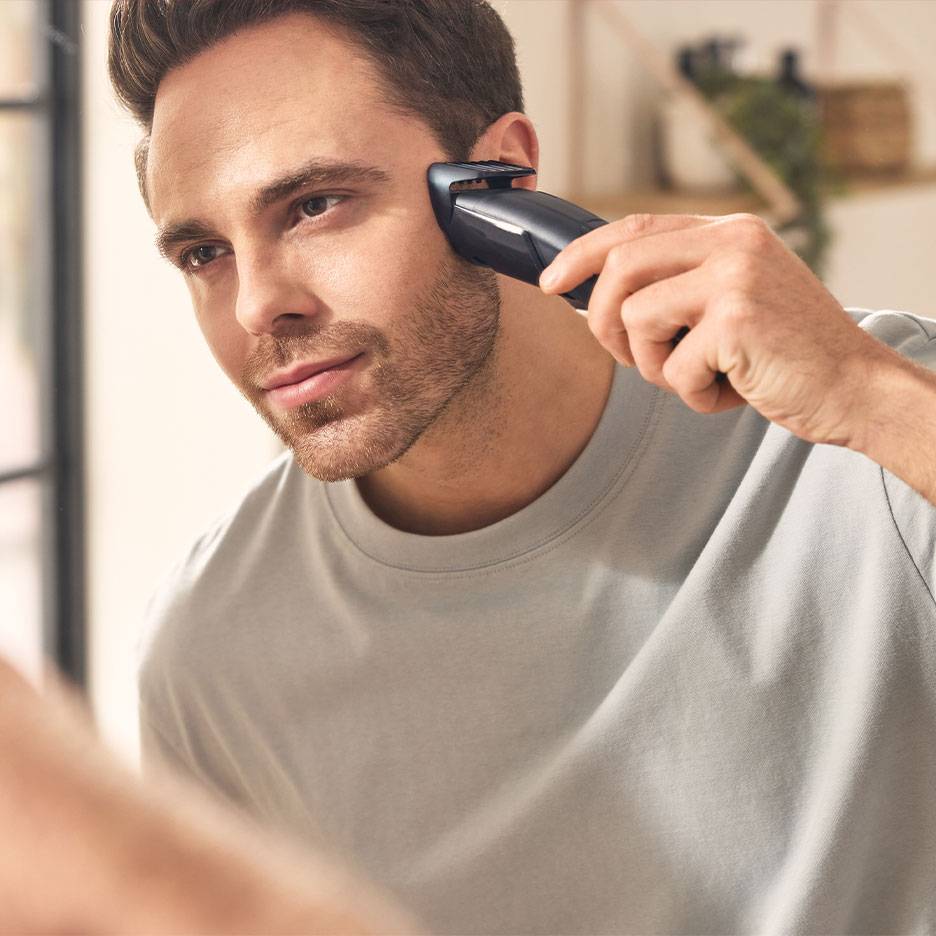 Man trimt zijn baard met een baardtrimmer voor de spiegel.