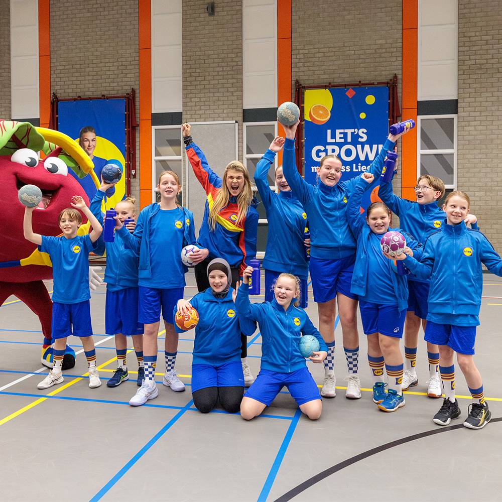 Groep kinderen en een volwassene in Lidl sportkleding met ballen en een mascotte.