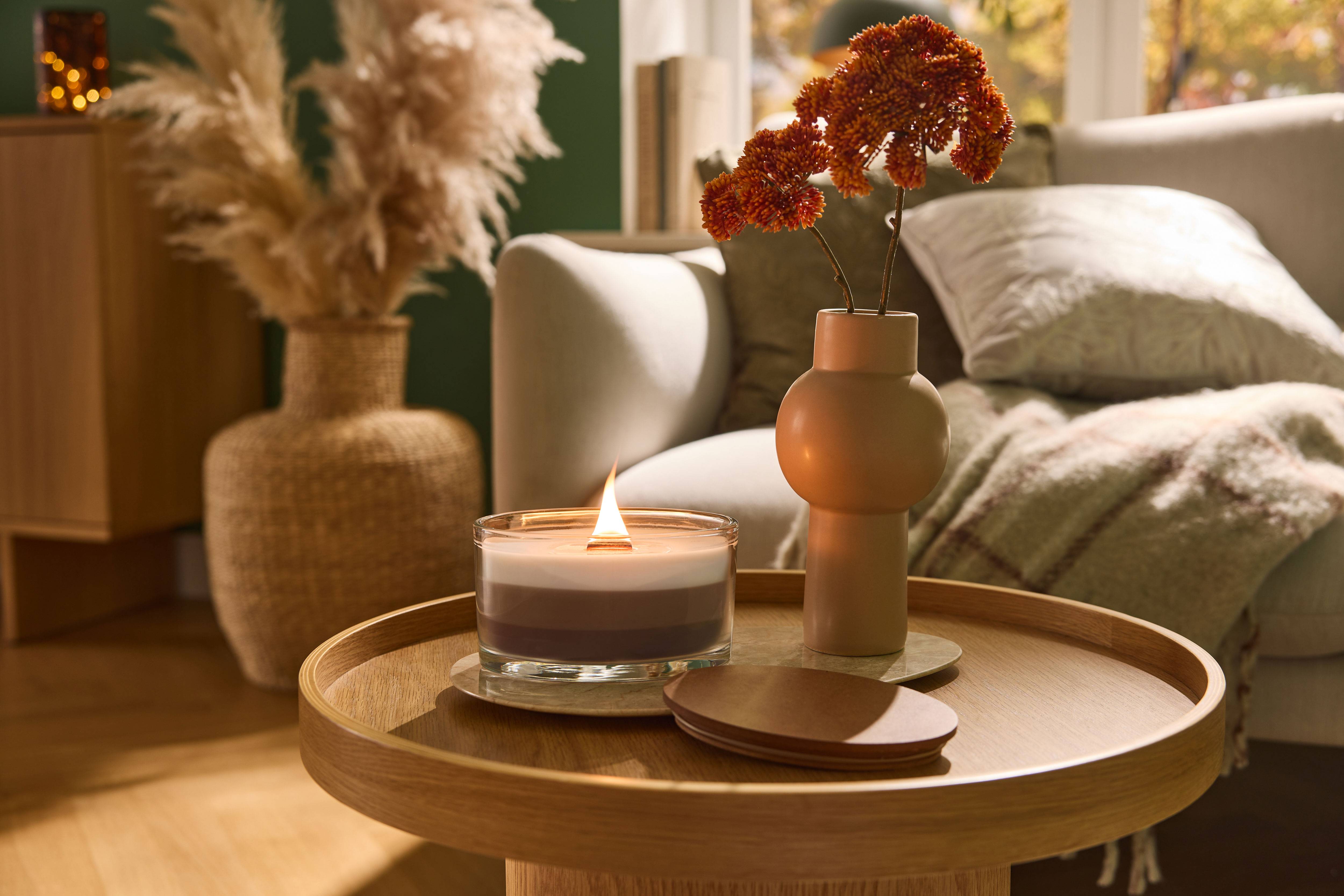 Brandende kaars en vaas met bloemen op een houten salontafel in de woonkamer.