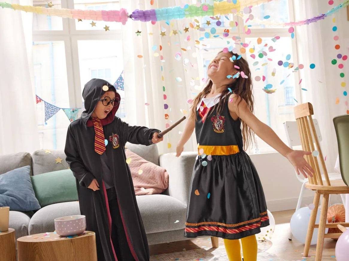 Twee kinderen verkleed als tovenaars, omringd door confetti en feestversiering.