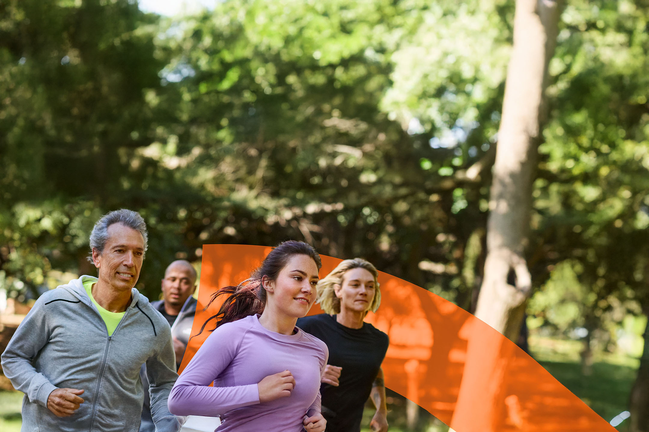 Vier hardlopers in sportkleding rennen buiten in een park.