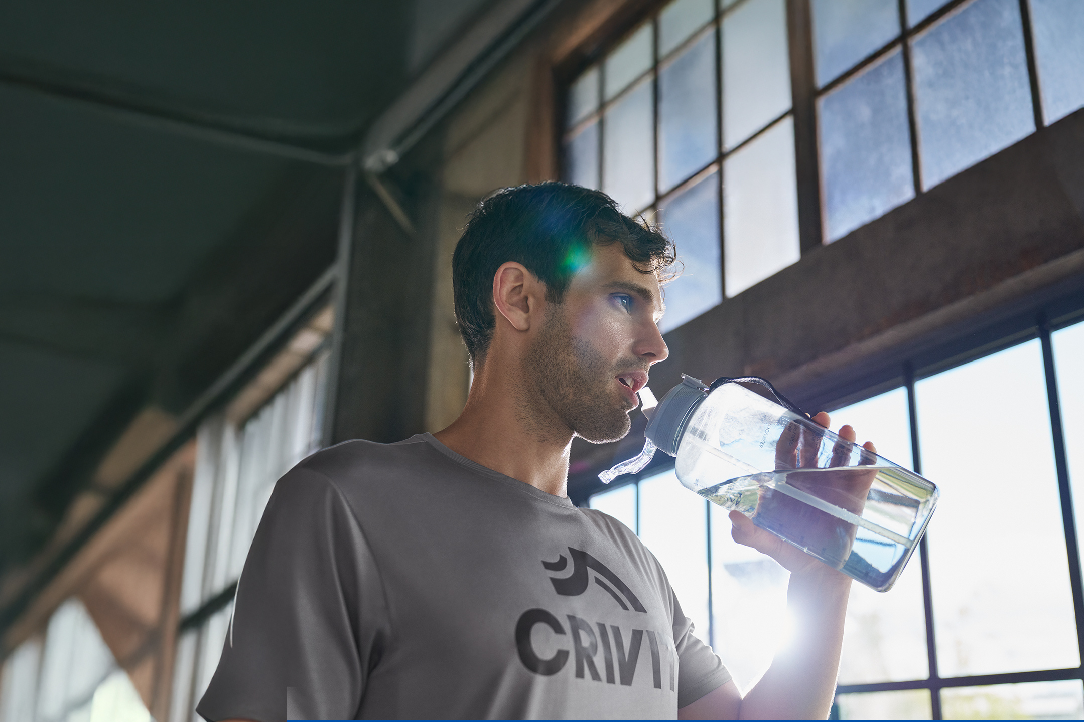 Man in een grijs sportshirt drinkt water uit een bidon.