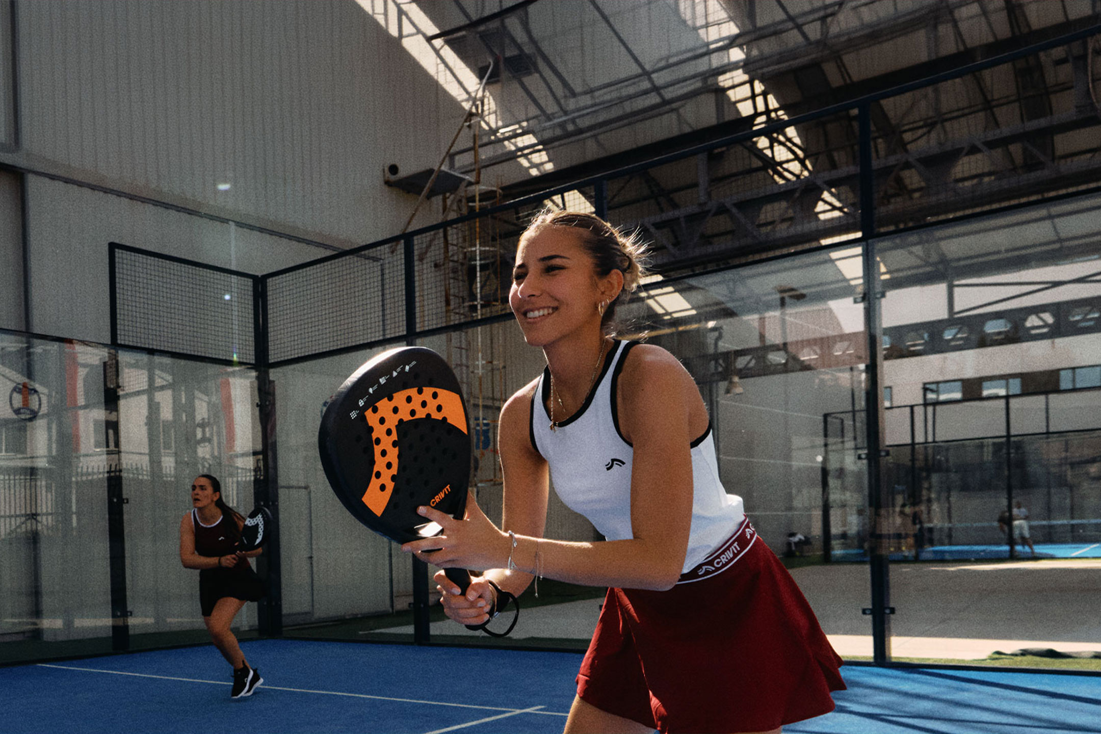 Gegenereerd door AI: Twee vrouwen spelen padeltennis, één lachend en een racket vasthoudend, op een blauwe baan.