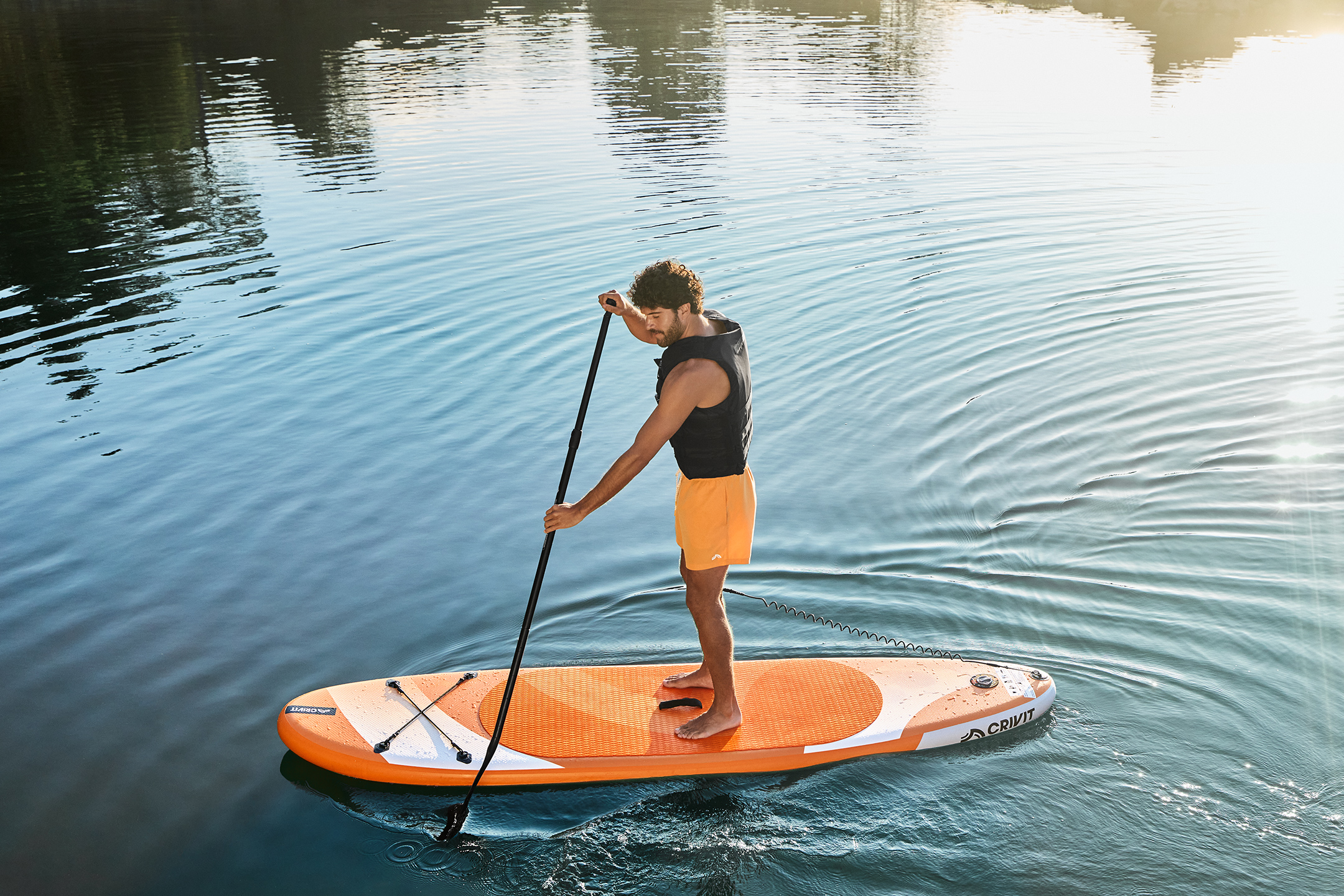 Man op een oranje paddleboard met peddel op rustig water.