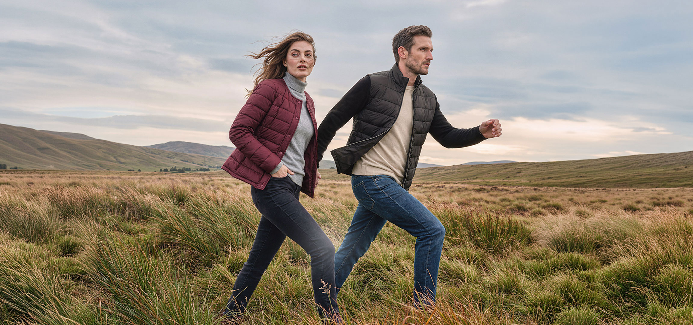 Gegenereerd door AI: Paar in lichte jassen en jeans wandelt door een glooiend graslandschap.