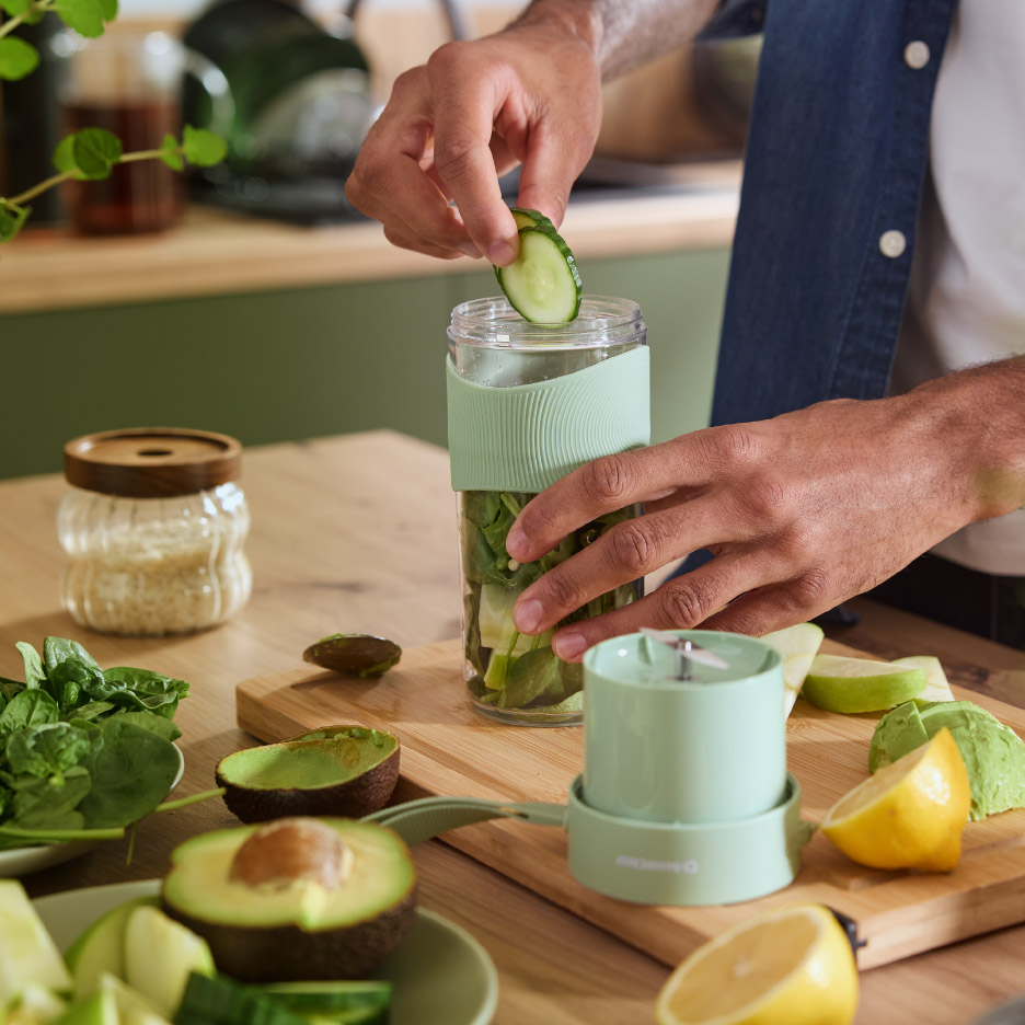 Man bereidt een groene smoothie met een draagbare blender, met avocado, spinazie en citroen.